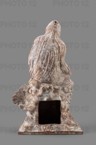 Figurine of Leda with a Swan, A woman sits on a rock and feeds a swan standing next to her. She is dressed in a cloak thrown over her head and back that falls along her body, completely enveloping her legs while leaving the rest of her body exposed. In her right hand, resting on her knees, she holds a platter; with her left arm bent and extended she holds it above the swan, which rests on her exposed hip with its head extended toward her. The woman bows her head and looks at the swan. The swan has outstretched wings. The woman's sandaled feet do not rest on the rock but dangle. The square base forms one with the rock. Cloak painted pink. Inscription/note: Maria Bernhard, 01.06.1942. Mid-3rd century BC, Myrina. Terracotta figurine, height 24 cm, width 15 cm, depth 12 cm, weight 0.56 kg., A weathered sculptural object is shown from the back, depicting a draped form seated on a textured base with rough, organic shapes and an empty rectangular cavity near the lower center; the surface show...