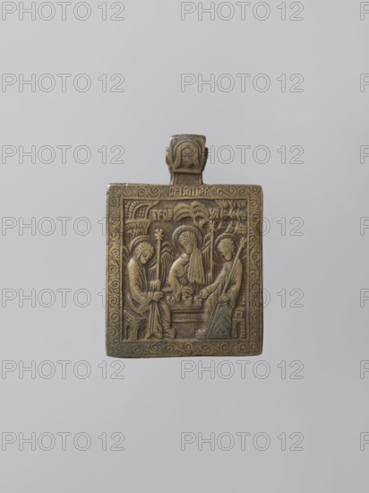 Icon: Old Testament Holy Trinity. Russian workshop; possibly Pomeranian workshop. Holy Trinity iconography with angels; Mandylion Not Made by Human Hands pendant; Angels with Abraham iconography. Small chest-worn icon depicting three angels holding scepters, seated behind a trapeze on which chalices stand and a prosphora lies. Background shows buildings, a tree, and a mountain. Surrounded by a floral ornament frame; stylized inscription Holy Trinity appears against the frame and below on both sides of the tree. Cast relief stylized and highly decorative; details and ornaments reference 16th–17th-century patterns. Likely from Pomeranian workshops. 18th century, Northern Russia possible place of manufacture. Icon; height 7 cm, width 4.8 cm., A small rectangular metal plaque with a tab at the top, rendered in bronze tones with areas of darker patina, sits against a pale gray background. The plaque's surface is carved in low relief showing a central scene with three seated human figures fa...