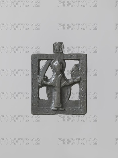 Icon: St. Nicholas. Russian workshop. Nicholas of Myra ca. 270–345/352. Icon depicting Saint Nicholas holding a sword in his right hand and a model of a city in his left. Proportions appear foreshortened; relief displays a clearly archaizing character. Background is cut out. Frame with a floral pattern; a small plaque with an image of the Mandylion placed on the axis. 2nd half of the 18th–19th century, Russia. Icon; height 7.5 cm, width 5.8 cm., A square dark gray metal relief with a raised central figure framed by a carved border, the figure wearing a robe and a halo-like headpiece and holding objects in each hand, with a small raised square projection at the top that contains a tiny carved face; the metal shows subtle variations in gray and a slightly reflective surface.