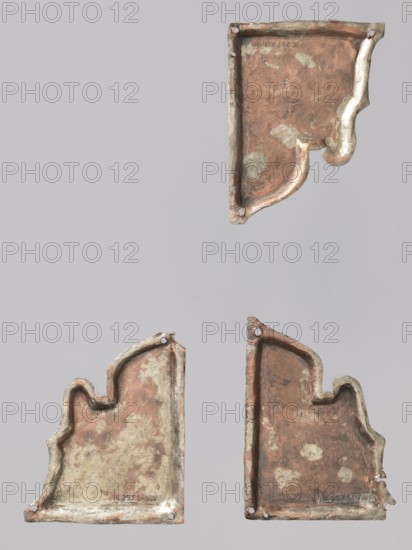 Three fragments of a Gospel book cover: two depict St. Mark and one St. Luke. Luke the Evangelist reaching for a pen; Mark with an open book; Mark sitting down to write with a pen. Inscribed; icon covers; book iconography; saints; evangelists. 17th–18th century, Russian; cover; height 9.4 cm, width 6.7 cm., Three irregularly shaped metal plates with worn, corroded surfaces are shown against a pale gray background. The plates have a mix of brownish copper and gray-green patina, with areas of lighter off-white corrosion. Each piece has rounded, sculpted edges and small round holes near some corners. The upper plate is oriented upside down relative to the two lower plates, which sit side by side with similar shapes and uneven, textured surfaces in brown, copper, gray, and off-white tones.