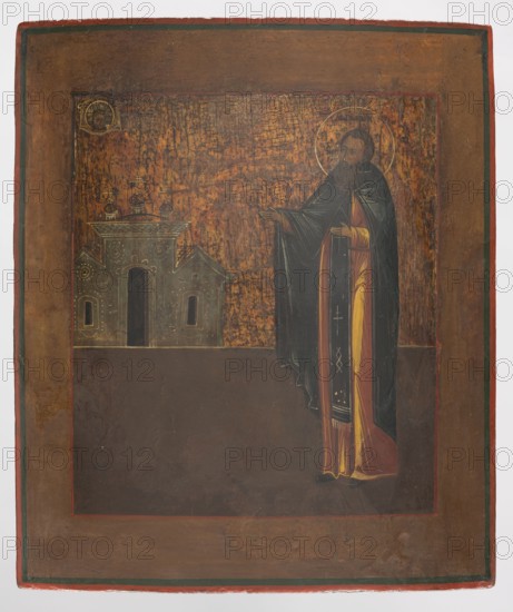 Icon: St. Monk Macarius. Provincial workshop. Icons; monks; Macarius Kalazinski St., 1400–1483 . Subjects: churches iconography, Jesus Christ Bible, Mandylion iconography, nimbus iconography, temples. Description: The icon shows the holy monk standing on the right in a gesture of prayer. On the left in the background are visible monastery buildings, and above them upper left an image of Acheiropoietos. The icon is quite schematic, in a manner characteristic of so-called poor icons. The saint's name is inscribed on his nimbus. Inscriptions workshop notes are engraved on the reverse of the icon. Date: 2nd half 19th century. Place: Russia. Medium: icon. Dimensions: height 35.8 cm; width 30.5 cm., A painted panel showing a standing robed figure with a halo, wearing dark outer robes and a yellow inner garment with red accents, extending an arm toward a small architectural group to the left; the architecture is rendered in muted greenish-gray with domed elements and arched openings. The back...