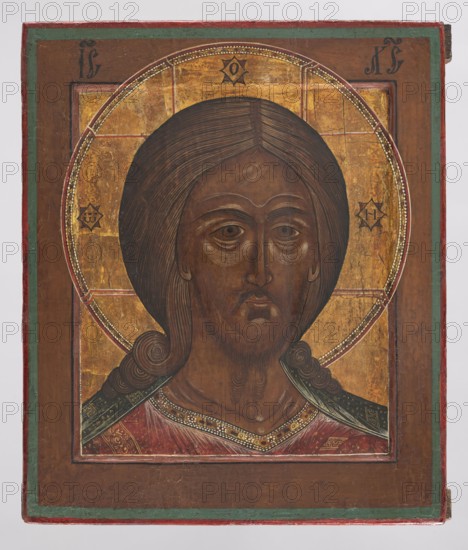 Icon: Christ the Savior. Old Believer Popovtsy workshop, Russian workshop. Subject: Jesus Christ. Medium/type: icon. Description: The face of Christ is depicted in the kovcheg with a brown complexion brightened by white tones on the forehead, eyelids, under the eyes, chin, and around the mouth. Eyes large; nose long and straight; hair parted in the middle, falling in circular locks on the shoulders; beard small and bipartite. Christ wears a red chiton with a gold border decorated with a delicate plant ornament, and a malachite himation with an ornament. Around the head is a cruciform halo; the letters on the arms of the cross are placed in double overlapping rhombuses—gold and red. The background of the kovcheg is gilded. Style linear, with tendencies toward decorativeness and stylization. Date: 2nd half of the 19th century. Place: Western Russia . Dimensions: height 31 cm, width 25.5 cm. Inscriptions: present. Iconography: star, halo., A painted panel showing a frontal portrait of a p...