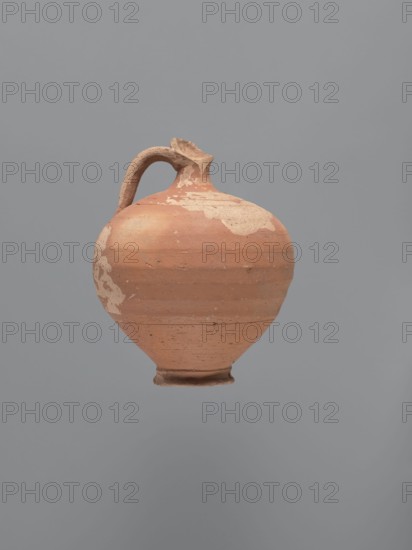 Jug, unknown Aswan workshop; type: jug; materials: kaolin clay Gempeler type IA with red-brown engobe exterior and beige-pink interior; form: rounded rim, narrow upwardly flaring neck with ring-shaped flange, spherical body with a large ribbon-shaped handle attached to lower body and middle of neck, ring-shaped foot; traces of turning slightly smoothed; style/technique: Aswan pottery / Egyptian sigillata / Coptic vessel; function: tableware vessel jug; date: 5th–6th century; find location: Edfu; dimensions: height 14.1 cm; lip diameter 2.4 cm; neck diameter 1.8 cm; body diameter 11.4 cm; base diameter 4.6 cm., An earthenware vessel with a rounded body and a small foot, shown against a plain gray background; the vessel is mostly terracotta orange with areas of lighter beige where the surface is worn, and it has a single curved handle attached near the top that is the same terracotta color with beige patches, a rough texture, and subtle horizontal banding around the body.