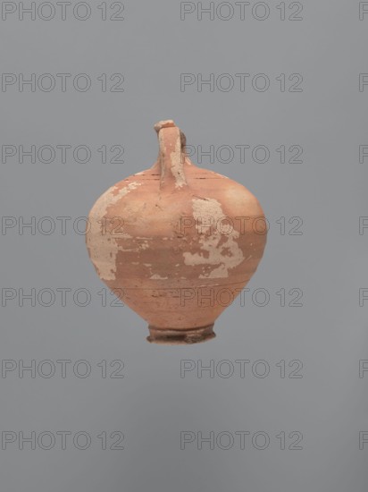 Jug, unknown Aswan workshop. Jug with a rounded rim, a narrow and upwardly flaring neck with a ring-shaped flange. Spherical body with a large ribbon-shaped handle attached to the lower part of the body and the middle part of the neck. Ring-shaped foot. Traces of turning slightly smoothed. Exterior covered with red-brown engobe, interior beige-pink, even. Kaolin ceramic mass Gempeler type IA. Egyptian sigillata / Egyptian pottery; Coptic vessels, tableware. 5th–6th century. Findspot: Edfu. Vessel jug. Height 14.1 cm; lip diameter 2.4 cm; neck diameter 1.8 cm; body diameter 11.4 cm; base diameter 4.6 cm., A single rounded ceramic vessel with a narrow neck and small flared foot is centered against a plain gray background; the vessel shows a weathered surface with patches of lighter worn areas and a base color of terracotta orange, with visible rough texture and small chips, and a few darker brownish spots and streaks.