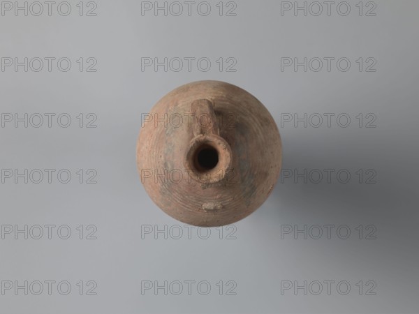Bottle, unknown Egyptian workshop. Bottle with a rounded and falling rim, concavely profiled. The almost cylindrical neck flows into rounded handles covered with fine ribs. Two handles one fragmentarily preserved are attached to the lower part of the neck and upper part of the shoulders. The ovoid body shows grooves on its lower part traces of turning; the base is ring-shaped. Outer surface brown and smoothed. Made of A4 marl clay with limestone inclusions. On the shoulders is faint painted decoration in black: two arcades composed of parallel arches separated by a row of dots, arranged symmetrically one between the handles. At the highest bulge of the body, below a damaged handle, there is an irregular concentration of a black substance, probably bitumen used to seal or repair the wall. Painted Coptic pottery/vessel, Coptic-style painted decoration. 6th century, Edfu. Vessel bottle. Height 22.7 cm; spout diameter 4.3 cm; neck diameter 3.0 cm; belly diameter 14.9 cm; bottom diameter 7....