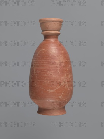 Bottle, unknown Aswan workshop; baggy-shaped bottle without a preserved spout. The neck widens toward the top with a circumferential bulge and another at its base; sloping shoulders; baggy belly flowing into the base on a low foot. Pink kaolin ceramic mass Gempeler IA. Partially smoothed turning marks visible on the surface. Outer walls covered with polished red engobe. 2nd half 5th–1st half 6th century. Find: Edfu. Vessel bottle. Height 20.6 cm; neck diameter 3.4 cm; body diameter 11.3 cm; bottom diameter 7.7 cm., A single terracotta vessel with a rounded body, a narrowed neck that flares into a short lip, and a small flared base, shown against a smooth gray background; the vessel displays a reddish-brown color with lighter beige marbling and surface streaks, with subtle variations of darker and lighter reddish-brown tones and a slightly matte texture.
