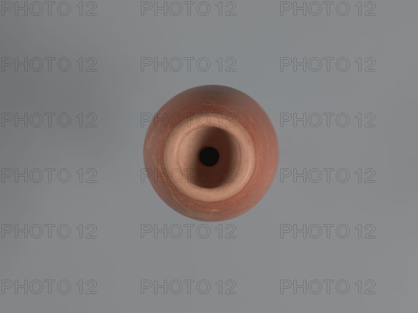 Bottle, unknown Aswan workshop; baggy-shaped bottle without a preserved spout. The neck widens toward the top with a circumferential bulge and another at its base. Sloping shoulders; belly is baggy, flowing into the base on a low foot. Pink kaolin ceramic mass Gempeler IA. Partially smoothed turning marks visible on the surface. Outer walls covered with polished red engobe. 2nd half 5th–1st half 6th century. Find location: Edfu. Vessel bottle. Height 20.6 cm; neck diameter 3.4 cm; body diameter 11.3 cm; bottom diameter 7.7 cm., A round clay vessel viewed from above showing a circular opening and an inner cavity, with a smooth rounded rim and visible concentric surface texture; the vessel is reddish-brown and terracotta in color with slightly lighter inner areas, and it sits against a flat, muted gray background.