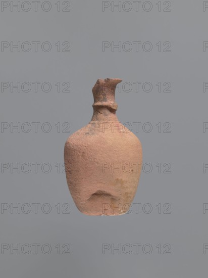 Jug, unknown Aswan workshop; jugs, tableware, Egyptian sigillata, Aswan pottery, Egyptian pottery, Coptic pottery. Kaolin clay, defective firing. Jug with a rounded and outward-turning rim, a cylindrical neck tapering at the base and provided with circumferential rollers midway up and at the base. Sloping shoulders merge into an ovoid belly. A preserved trace of a vise indicates it connected the middle of the neck with the upper part of the shoulders. Flat bottom, curved inward. Pink kaolin ceramic body Gempler IA. Surfaces eroded, but remnants of a yellow engobe survive in the bottom section. Below the vice attachment point, on the left side near the bottom, a dent in the wall is visible, probably from a firing error. 5th–7th century, Edfu find location. Vessel, jug. Height 15.7+ cm preserved; rim dia. 5.0 cm; neck dia. 2.4 cm; body dia. 9.7 cm; bottom dia. 4.0 cm., An earthenware vessel with a rough, textured surface in shades of terracotta, ochre, and muted brown floats against a pl...