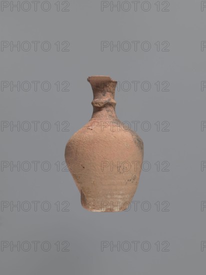 Jug, unknown Aswan workshop, jugs, tableware, Egyptian sigillata, tableware, Aswan pottery, Egyptian pottery, Coptic pottery, kaolin clay, defective firing. Jug with a rounded and outward-turning rim, a cylindrical neck, tapering at the base and provided with circumferential rollers midway up and at the base. Sloping shoulders merge into an ovoid belly. A preserved trace of a vise indicates that it connected the middle part of the neck with the upper part of the shoulders. Flat bottom, curved inward. Pink kaolin ceramic body Gempler IA. Surfaces eroded, but remnants of a yellow engobe have survived in the bottom section. Below the vice attachment point, on the left side near the bottom, a dent in the wall is visible, probably the result of a firing error. 5th–7th century, Edfu, vessel, jug. Height 15.7+ cm preserved; diameter 5.0 cm rim; diameter 2.4 cm neck; diameter 9.7 cm body; diameter 4.0 cm bottom., A single clay vessel with a rounded body and a narrow neck is centered against a ...