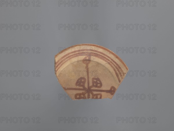 Shallow bowl with a rounded rim, inversely trapezoidal, parted walls, and a flat bottom. Pink kaolin ceramic mass Gempler IA with yellow, even surfaces. Decoration painted in red: a circumferential band on the rim and a central composition on the interior, bounded by three parallel circumferential bands midway up the wall. Central eight-pointed rosette motif of alternating long and short lines, each ending with a geometric flower in the form of an oval filled with intersecting lines. Painted Coptic/Nubian-style vessel, 8th–9th century, from Edfu. Vessel bowl; height 3.2 cm; diameter 16 cm rim, 6.4 cm base. Maker/place of origin: unknown Aswan workshop. Materials: kaolin clay; painted ceramic., A fragment of pottery with a tan base and reddish-brown painted decoration sits against a smooth gray background. The pottery shard shows a curved rim with a few concentric reddish-brown bands and a painted central motif consisting of intersecting lines and four petal-like shapes in the same redd...