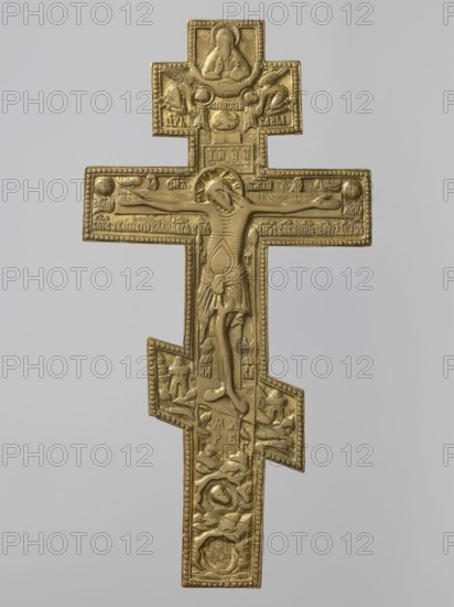 Cross: Crucifixion of Christ; Old Believers workshop. Subjects and iconography: Adam Bible, angels, Jesus Christ Bible, God the Father iconography, the Holy Spirit iconography, skull iconography, crosses, moon iconography, Lord of Hosts iconography, Jerusalem Israel/Palestine, sun iconography, Dove Bible. Description: The obverse presents iconography typical of Old Believers/Pop-Rites crosses: the crucified Christ, above him the Lord of Hosts blessing from the clouds, below him the dove of the Holy Spirit flanked by angels descending toward the Savior. The cross stands on symbolic Golgotha with a cave containing Adam’s skull and is shown against a symbolic representation of Jerusalem. On the reverse is an apotropaic prayer to the Holy Cross. 19th century, Russia. Medium: cross; height 36.5 cm, width 18.5 cm., A gold-colored metal cross with ornate relief carving depicting a central figure on the main horizontal arm and additional carved scenes above and below, showing a larger top sect...