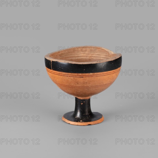 Fragment of a lydion, Archaic period. Fragmentarily preserved lydion foot and lower part of the body. The foot is flat, disc-shaped, conically recessed at the bottom in the middle. The medium-high, cylindrical foot tapers slightly towards the bowl. The bowl, in the preserved part, is hemispherical. The top of the foot, the foot, and the upper parts of the bowl are covered with a glossy varnish; remaining parts are clay-colored. The outer surface of the bowl is decorated with four horizontally arranged thin lines in light brown. The interior of the bowl is not smoothed, with visible traces of turning. The outer part of the foot is covered with matte varnish. Varnish color: 10 YR 2/1 black Ornament color: 2.5 YR 4/3 reddish brown; 2.5 YR 4/6 red Color of clay: 5 YR 6/6 reddish yellow Attributed to Asia Minor possibly Lydia; lydion type, vessel. Dated to the 2nd half of the 6th century BC analogies suggest c. 550–525 BC. Height 7 cm, width 7.7 cm, weight 0.132 kg., A ceramic bowl on a sho...