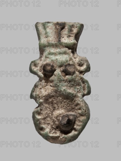 Amulet — single-sided tile with a schematic relief representation of Bes: a head with a feathered crown and a shield with a phallus . Eyes and phallus applied with black glaze. Amulet, plaster/ceramic tile. Late Period–Ptolemaic period, 7th–1st century BC, Egypt. Height 2.7 cm; width 1.3 cm., An irregularly shaped object with a rough, pitted surface in shades of tan, brown, and green is shown against a neutral gray background; the form has a wider top that tapers slightly and then bulges into rounded protrusions along the sides, with a pair of raised rounded bumps near the upper middle and another rounded protrusion lower down, and the surface shows grainy texture, erosion, and patches where the tan and brown mix with muted green.