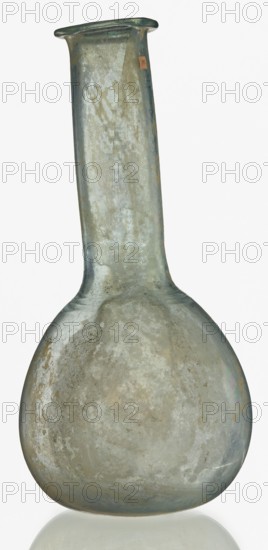 Pear-shaped vial, unknown Eastern workshop. The body is a slightly elongated sphere with a flattened bottom. The neck is long, exceeding the height of the body, cylindrical, ending with an outwardly curled horizontal rim. The surface on both sides of the joint between the body and the neck is decorated with a thin, grooved spiral line. 1st–2nd century, Roman Empire 27 BC–476. Vessel; height 17.5 cm, width 8.5 cm., A glass vessel with a rounded body and a long cylindrical neck topped by a flared rim, mostly translucent with weathered, cloudy surface textures and a mottled appearance in shades of pale green, gray, and muted blue, with areas of off-white and beige staining and faint iridescent sheen.