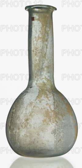 Pear-shaped vial, unknown Eastern workshop. The body is a slightly elongated sphere with a flattened bottom. The neck is long, exceeding the height of the body, cylindrical, ending with an outwardly curled horizontal rim. The surface on both sides of the joint between the body and the neck is decorated with a thin, grooved, spiral line. 1st–2nd century, Roman Empire 27 BC–476. Vessel; height 17.5 cm, width 8.5 cm., A glass bottle with a rounded base and a long narrow neck, showing an aged surface with patches of worn finish in pale gray, beige, light brown, muted green, and hints of blue; the glass has a slightly cloudy, weathered appearance with irregular speckling and peeling areas, and the rim is flared and thicker than the neck.
