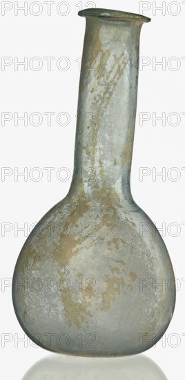 Pear-shaped vial, unknown Eastern workshop. The body is a slightly elongated sphere with a flattened bottom. The long cylindrical neck exceeds the height of the body and ends with an outwardly curled horizontal rim. The surface on both sides of the joint between body and neck is decorated with a thin, grooved spiral line. 1st–2nd century, Roman Empire 27 BC–476. Vessel; height 17.5 cm, width 8.5 cm., A rounded bottle with a long narrow neck and a flared rim, showing irregular patches and streaks of muted green, gray, and tan across its surface, with a slightly translucent, weathered appearance and subtle reflections at its base.