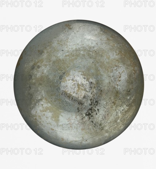 Pear-shaped vial, unknown Eastern workshop. The body is a slightly elongated sphere with a flattened bottom. The neck is long, exceeding the height of the body, cylindrical, ending with an outwardly curled horizontal rim. The surface on both sides of the junction between body and neck is decorated with a thin, grooved spiral line. 1st–2nd century, Roman Empire 27 BC–476. Vessel. Height 17.5 cm; width 8.5 cm., A large round metallic object fills the frame, showing a weathered, pitted surface with areas of worn paint and patchy corrosion. The visible colors include silvery gray, dull silver, pale blue-gray, muted greenish-gray, and patches of brownish rust and tan. The surface has a mottled texture with areas of smooth sheen, flaky discoloration, and irregular darker spots, creating a marbled, uneven appearance across the circular form.