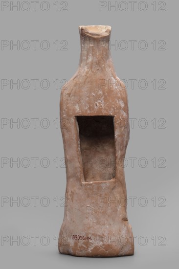 Figurine of a woman wearing a polos, from an unknown Boeotian workshop; female figurine, Boeotia, 475–450 BC; terracotta sculpture, height 26 cm, width 9 cm, depth 7 cm, weight 0.43 kg., A tall, upright ceramic object with a narrow neck and a wider body, showing a rough, weathered surface in shades of terracotta, brown, and beige with whitish scuff marks, featuring a rectangular hollow cavity carved into the front that reveals a darker, earthy interior, with irregular contours and worn edges and a muted gray background.