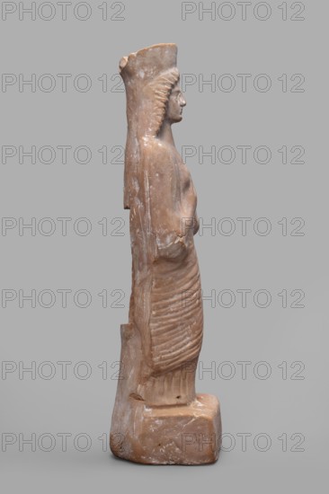 Figurine of a woman with a polos on her head, unknown Boeotian workshop, female figurine, 475–450 BC, Boeotia; sculpture; height 26 cm, width 9 cm, depth 7 cm, weight 0.43 kg., A weathered terracotta figure with a reddish-brown surface stands on a rectangular base, shown in profile facing right; the figure wears a tall headpiece and a long, vertically ribbed garment that falls to the base, and there is visible surface abrasion and lighter worn patches across the body and base, with overall colors including reddish-brown, pale beige highlights, and a neutral gray background.