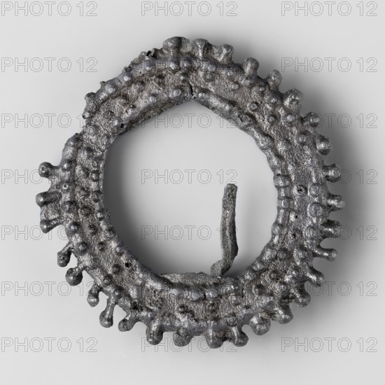 Miniature brooch, votive offerings, wreaths, 1st–2nd century, Roman Empire 27 BC–476, toy, amulet; height 4.6 cm, width 0.9 cm, weight 0.018 kg, A roughly circular metallic object with a textured, bumpy surface and irregular protrusions around its outer edge, shown against a smooth light gray background; the object appears dark gray with silvery highlights and a slightly rough, pitted finish, and there is a thin, vertical metallic fragment rising from the inner edge.