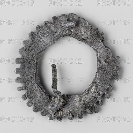 Miniature brooch, votive offering/wreath, 1st–2nd century, Roman Empire 27 BC–476, toy/amulet; height 4.6 cm, width 0.9 cm, weight 0.018 kg., A roughly circular metallic object with an irregular toothed outer edge and a hollow center, showing a heavily textured, pitted surface with rough, uneven protrusions and a broken, jagged inner ring; the object displays shades of gray, silver, dark gray, and black against a light gray background.