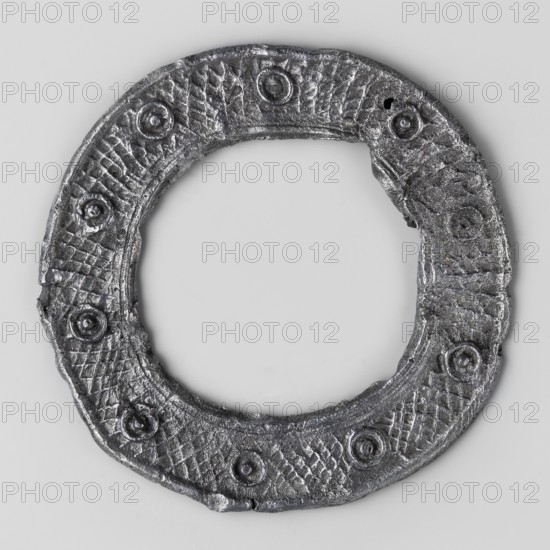 Miniature brooch, votive offering/wreath, object in the shape of a flat hoop with a surface decorated with a mesh ornament and circles with a knob in the middle, 1st–2nd century AD, Roman Empire 27 BC–476, amulet/toy, height 5.6 cm, width 0.3 cm, weight 0.014 kg, A circular metallic ring with a rough textured surface and a dark gray to silver color, featuring a few raised circular bosses spaced around the band and a repeating crosshatched pattern between them, set against a light gray background.