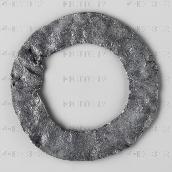 Miniature brooch, votive offering/wreath; object in the shape of a flat hoop with a surface decorated with a mesh ornament and circles with a knob in the middle; 1st–2nd century AD, Roman Empire 27 BC–476; amulet/toy; height 5.6 cm, width 0.3 cm, weight 0.014 kg, A circular metal ring with an irregular, rough texture lies flat against a light gray background; the ring shows a worn, pitted surface with uneven edges and a few small indentations, and its color appears predominantly dark gray with lighter silver-gray highlights where the surface catches light.