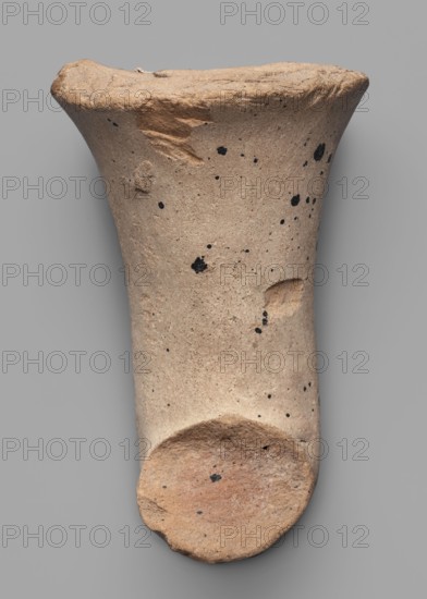 Fragment of a transport amphora body stamped with a Rose of Rhodes, unknown Rhodian workshop; stamp impressions; trade. Fragment of a transport amphora stamped with a Rose of Rhodes and the inscription Chresimou, ca. 280–ca. 220 BC, Rhodes; vessel stamped body, height 6.8 cm, width 10 cm, A roughly cylindrical, tapered object with a flared rim and a rounded base displayed against a neutral gray background; the surface is a sandy beige with scattered small black speckles and a few darker spots, and there are areas of slightly darker brownish-beige where the texture appears rougher or chipped, including a small indentation on one side and a worn, uneven rim.