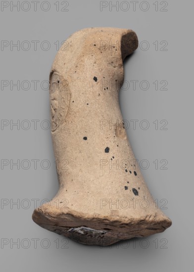 Fragment of a transport amphora neck stamped with a Rose of Rhodes, unknown Rhodian workshop; stamp impressions; trade; fragment stamped with a Rose of Rhodes and the inscription Chresimou; ca. 280–ca. 220 BC; Rhodes; vessel stamped neck; height 6.8 cm, width 10 cm, A weathered, curved ceramic fragment in beige and light tan tones with a rough, pitted surface and several small black speckles scattered across it, showing a rounded top and a flared base with a chipped, uneven edge; the fragment includes a faint raised circular imprint on one side and areas of darker brown discoloration near the rim, all set against a plain gray background.