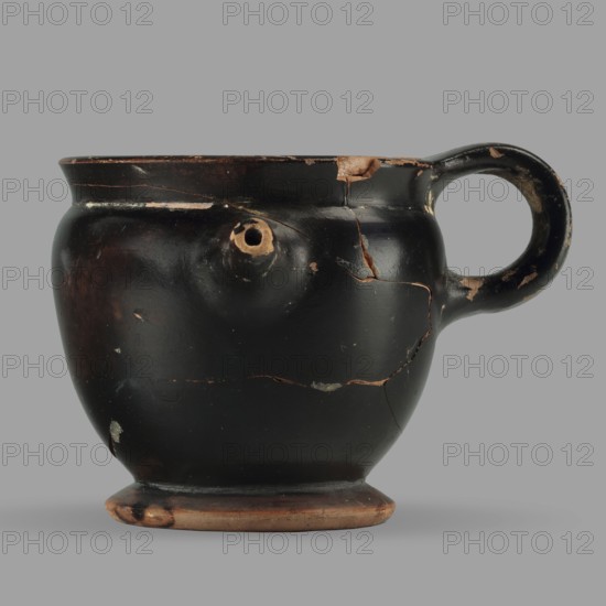 Askos with spout and strainer, unknown Attic workshop, Greek pottery toilet vessel with tubular spout and ribbon handle; top covered with a strainer. 5th century BC, Attica; vessel askos. Height 6.2 cm, width 8.3 cm, depth 9 cm, weight 0.09 kg., A rounded ceramic vessel with a single loop handle and a small protruding spout, shown against a flat gray background; the vessel has a glossy black surface with areas of worn brownish-orange clay visible where the black coating has chipped, and several hairline cracks and missing flakes revealing the brownish-orange beneath; the base shows exposed brownish-orange clay with darkened spots, and the handle interior has worn lighter areas; overall colors visible include black, brownish-orange, and gray.