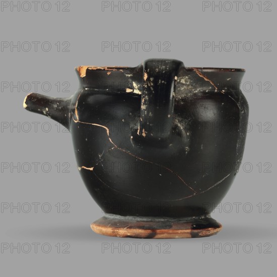 Askos with spout and strainer, unknown Attic workshop, Greek pottery toilet vessel with tubular spout and ribbon handle; top covered with a strainer. 5th century BC, Attica; vessel askos. Height 6.2 cm, width 8.3 cm, depth 9 cm, weight 0.09 kg., A dark rounded ceramic vessel with a short spout on one side and a stout handle on the opposite side, showing a matte black surface with worn areas where a warm terracotta color is exposed; the rim and foot show chipping revealing the same terracotta tone, and several fine cracks and repaired lines traverse the body; the handle and spout display scuffed spots and small abrasions, and the object sits against a flat neutral gray background.