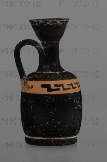 Black-finned aryballois lekythos. Large, ring-shaped foot. The body is rather squat, barrel-shaped with rounded shoulders. The neck is quite narrow, clearly separated from the body and the flaring rim. In the upper part of the body there is a slightly irregular clay-colored orange band not covered with black finish; on it, at the front, a rather carelessly executed meander interrupted with black paint. The upper part of the device is tilted to the left. Black-finned pottery, lekythos. Condition: minor chips, rim edge worn. 4th century BC 1st half of the 19th century noted, unknown place of origin. Vessel height 10.9 cm, diameter 5.4 cm., A single ceramic vessel with a handle and narrow neck sits against a gray background; the vessel is primarily black with a band of orange-beige around its shoulder that contains a repeating dark decorative motif, and the surface shows areas of wear and small pale flecks; the handle and rim also show worn black paint revealing the orange-beige beneath, ...