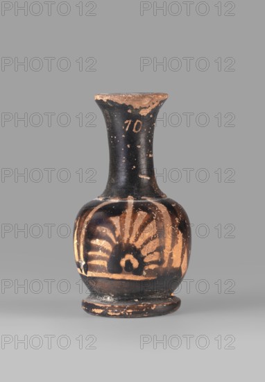 Miniature red-figure lekythos decorated with a palmette;,  repossession Silesia; red-figure pottery; lekythos; early 4th century BC; Attica place of origin; vessel; height 7.4 cm; width 4.5 cm., A small rounded ceramic vessel with a narrow neck and flared rim set against a plain gray background, showing a worn black surface with exposed terracotta areas and a decorative sunburst-like motif on its bulbous body in the terracotta color; the neck and rim show chipped black glaze revealing the underlying lighter material, and the base is slightly raised with similar wear and patches of black and terracotta.