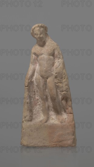 Terracotta figurine of Heracles, terracotta, figurines of nude men, Heracles mythology, Greek mythology, figurines made of molds. Figurine of a standing naked Heracles in a contrapposto pose. He has a cloak thrown over his back. His right hand rests on a rock, and in his left he probably holds a club. Condition of preservation: good. 2nd–1st century BC. Asia Minor. Figurine, height 14.3 cm., A small weathered statue of a standing human figure carved from a stone-like material, shown against a plain gray background. The figure appears to wear a draped cloth over one shoulder and arm, with the other arm and torso more exposed. The surface shows rough texture and erosion, with patches of pale beige, light brown, and muted pinkish tones, and small areas of darker brown and faint yellowish discoloration. The base is blocky and rectangular with a similar rough surface and color variation, including pale beige and terra-cotta hues. The figure's head is slightly tilted with indistinct facial f...