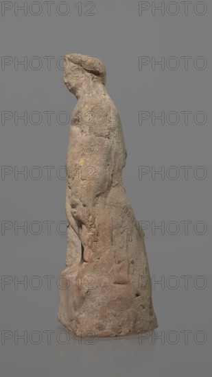 Terracotta figurine of Heracles, terracotta, figurines of nude men, Heracles mythology, Greek mythology, figurines made of molds. Figurine of a standing naked Heracles in a contrapposto pose with a cloak thrown over his back. His right hand rests on a rock, and in his left he probably holds a club. Condition of preservation: good. 2nd–1st century BC, Asia Minor, figurine, height 14.3 cm, A worn stone figurine of a standing person shown in profile on a neutral gray background, the figure carved with a rounded head, a suggestion of facial features, and a short hairstyle or head covering; the body appears clothed with a draped form extending to a square base, showing surface weathering, small pits, and abrasions; the stone displays tones of beige, tan, light brown, pale pink, and traces of yellow and greenish discoloration, with faint white veining and patches of darker brown.