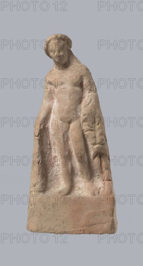 Terracotta figurine of Heracles. Figurine of a standing naked Heracles in a contrapposto pose; cloak thrown over his back. His right hand rests on a rock, and in his left he probably holds a club. Terracotta, made from a mold. Figurines of nude men; Heracles Greek mythology. Condition of preservation: good. 2nd–1st century BC. Asia Minor. Height 14.3 cm., A weathered stone sculpture of a standing human figure on a rectangular base, showing a simplified torso, limbs, and head with softened facial features, drapery or cloak hanging behind and to the sides, and a rough, pitted surface texture; visible colors include beige, light brown, pale pink, and hints of gray.