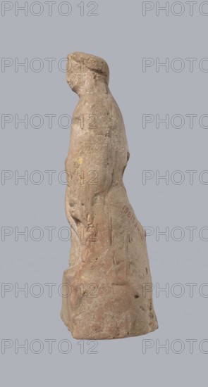 Terracotta figurine of Heracles, terracotta, figurines of nude men, Heracles mythology, Greek mythology, figurines made of molds. Figurine of a standing naked Heracles in a contrapposto pose with a cloak thrown over his back; his right hand rests on a rock and in his left he probably holds a club. Condition of preservation: good. 2nd–1st century BC, Asia Minor, height 14.3 cm., A weathered stone figure shown in profile against a plain gray background, with a rounded head and simplified facial features, a sloping back, and an overall elongated, upright silhouette; the surface shows rough texture, scratches, and chips with areas of worn patina and faint traces of color in shades of light tan, beige, pale pink, muted brown, and small hints of yellow.