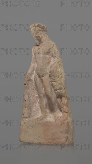 Terracotta figurine of Heracles, terracotta, figurines of nude men, Heracles mythology, Greek mythology, figurines made of molds. Figurine of a standing naked Heracles in a contrapposto pose. He has a cloak thrown over his back. His right hand rests on a rock, and in his left he probably holds a club. Condition of preservation: good. 2nd–1st century BC, Asia Minor, figurine, height 14.3 cm., A weathered stone sculpture of a standing nude figure with a rounded head and downturned gaze, carved in a rough, textured style and attached to a block-like base; the figure appears to have a cloak or drapery hanging from the shoulders and along one side, with visible surface erosion and tool marks. The colors visible are muted tan, beige, pale pink, light brown, and hints of gray and yellow against a solid gray background.