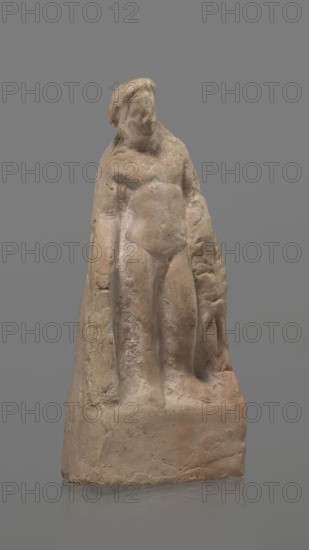 Terracotta figurine of Heracles, terracotta, figurines of nude men, Heracles mythology, Greek mythology, figurines made of molds. Figurine of a standing naked Heracles in a contrapposto pose. He has a cloak thrown over his back. His right hand rests on a rock, and in his left he probably holds a club. Condition of preservation: good. 2nd–1st century BC, Asia Minor, figurine, height 14.3 cm., A small weathered sculpture of a standing human figure carved from a light brownish-beige stone with traces of pale pink and gray, shown against a uniform gray background; the figure wears a cloak-like drapery that falls along the sides, has a rounded head with softened facial features, a torso with subtle muscle and belly contours, and legs set close together on a rectangular base that shares the same light brown-beige and pale pink coloration and shows surface roughness and small pits.