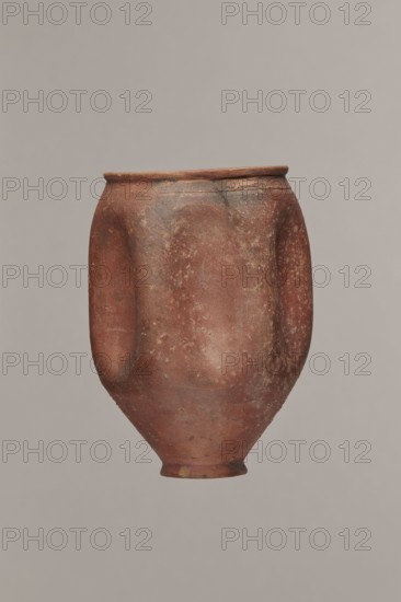 Rippled beaker miniature version, unknown Germanic workshop from Cologne?, hard-fired fine-grained clay with small content of silvery mica, buff-pink-brown 5YR 6/4–6/6; grey-olive matte glaze 5YR 4/1–4/2 covering the entire surface, exterior slightly rough intentionally sandblasted; lower part above the foot shows glaze discolorations from fingerprints. Walls have six decorative dents. Minor damage to the rim, slight cracks. 2nd half of the 2nd–3rd century; likely Cologne; vessel, height 9.7 cm, diameter 5.5 cm., A single rounded clay vessel with a narrow base and flared rim fills the frame, showing a textured surface with worn patches and irregular speckling; the form has subtle vertical indentations on its sides and a slightly uneven lip. The visible colors are reddish-brown with areas of darker brown, muted tan, and small flecks of lighter beige, set against a soft gray-beige background.