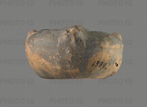 Oil lamp, unknown Gaulish workshop, repossession Frombork; Warmian-Masurian Voivodeship, oil lamp, single-burner lamp, Roman lamp, Buchi type IX-b = Loeschcke type IXb oil lamp. Lamp from a mold. Round vessel. Arms sloping outward, separated from the disc by a convex edge. Two bars arranged symmetrically on the arms. One vertically placed vice opposite the burner also from a mold, broken off. Concave, flat disc with one large centrally located olive hole. Medium-length wick channel, decorated with a groove in the center. Two small air ventilation holes at either end of the groove. Rounded end of the burner. Large wick hole. No charring. 1st century, Gaul, height 3.7 cm, width 10.9 cm, depth 7 cm, A rounded, irregularly shaped object with a rough, pitted surface rests against a plain background; its surface shows a mix of gray and brown tones with areas of darker gray and patches of lighter, sandy brown, and small spots of pale discoloration; the object has several protrusions and inden...