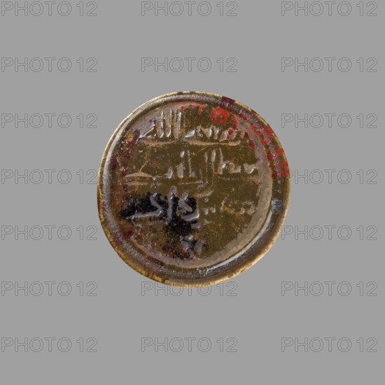 Weight; creator, role/classification: craftsman; provenance, Islamic art; Arabic culture; Islam; Fatimid dynasty 909–1171; inscriptions in Arabic; 11th–12th century; Egypt; object: weight; weight 1.23 g; diameter 2.6 cm; height 2.6 cm; diameter 1.9 cm, A circular metallic object with a worn, reflective surface placed against a plain gray background, showing a patina of brownish-gold with areas of darker brown and black discoloration, a few red spots near the edge, and some lighter silvery highlights along the rim and raised areas.