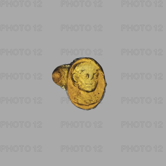 Gemma intaglio with a portrait of a boy, unknown Italian workshop, portraits of boys, 1st half of the 1st century, Italy, Roman Empire 27 BC–476, gemma; height 1.1 cm, width 1.2 cm, depth 0.3 cm, A small amber-colored oval object with a raised relief of a humanlike face sits against a flat gray background; the object shows darker amber tones around its edges and a few lighter yellowish highlights on its raised surfaces, and there is a rounded protrusion attached to one side with a slightly more brownish-amber hue.