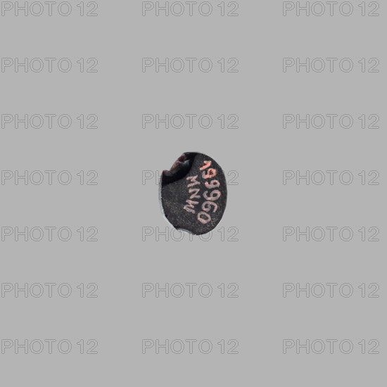 Gemma cameo with a representation of a woman's head, unknown Roman workshop, female portrait, 3rd century, Roman Empire 27 BC–476, gemma; height 1 cm, width 0.8 cm, depth 0.3 cm, A small circular dark object sits near the center of a plain light gray background; the object appears mostly black with a rough texture and has a few worn or chipped edges revealing a lighter gray beneath, and there are traces of a faded pinkish color on its surface.