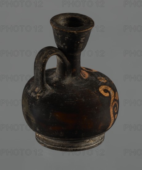Red-figure aryballos lekythos, unknown Campanian workshop. A squat lekythos with a ring-shaped foot. The belly is broad, spherical, and flattened; the shoulders are rounded and broad. The narrow, low neck is as high as the rim. The rim is cup-shaped. The handle is ribbon-shaped, vertical. The front is decorated with a bar ornament at the base of the neck. The belly and arms depict a seated woman facing left: legs in profile left extended, right withdrawn, hips three-quarters en face, arms frontal, head in left profile. The left arm is wrapped around a himation, the hand resting on the hip; the right hand is outstretched, above which lies a tossed circular object of two light-colored parts ball or skein of wool?, each with a single black dot and separated by a dark stripe. Hair combed back and tied in a bun; woman wears a necklace and spherical-bead earrings depicted with dots. Sides feature vertically unwinding plant tendrils with spirally coiled ends. Reddish clay; turning lines visib...