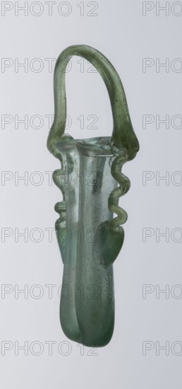 Dilekyt, unknown Eastern workshop Syrian or Palestinian, gift, reinventory; glass vessel, Roman Empire, 3rd century. The vessel consists of two tubes connected at one side and a flat bottom. The outer sides are gently curved towards the axis and decorated with two thick glass threads. The wavy threads begin with thickenings at one-third of the vessel's height and terminate at the rings of the slightly flared spouts. At the joints of the threads and spouts, a large bow-shaped vice is supported, wider on one side than the other, narrowed at the top. Height 15.7 cm; width 7.3 cm; depth 2.3 cm., A translucent green glass vessel with a rounded loop handle and an elongated body, showing a smooth, slightly bubbled surface and a few irregularities; the handle arches from the rim and the sides feature wavy, ribbon-like protrusions and bulbous accents, with the glass varying between pale green and deeper green tones against a light grey background.