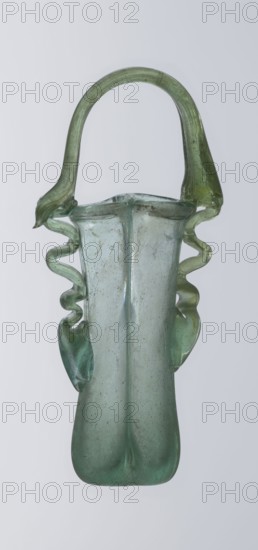Dilekyt, unknown Eastern workshop Syrian or Palestinian, glass vessel, 3rd century, Roman Empire 27 BC–476, two tubes connected at one side with a flat bottom. Outer sides gently curved toward the axis and decorated with two thick wavy glass threads that begin with thickenings at one-third height and terminate at the rings of slightly flared spouts. At the joints of the threads and spouts, a large bow-shaped vice is supported, wider on one side than the other, narrowed at the top. Height 15.7 cm, width 7.3 cm, depth 2.3 cm., A translucent glass vessel in shades of pale green and seafoam green with a tall narrow body that widens slightly toward the top, a curved arching handle attached at the rim, and decorative undulating glass ribbons running down both sides; the glass shows slight cloudiness and small surface irregularities, and the background is a uniform pale gray.