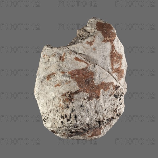 Fragment of a stucco mask. Lower part of the face of a bearded man; preserved are the chin, mouth, cheeks, and part of the nose. Sarcophagus mask, 2nd century, Roman period, Egypt. Height 11.7 cm; width 8.7 cm., A roughly oval stone with a rough, pitted surface sits against a flat gray background; the stone shows a base color of light gray and off-white with patches and streaks of reddish-brown and small areas of darker gray to black speckling, and its surface texture includes cracks, ridges, and uneven indentations with a few areas that appear smoother and a few that look more granular.