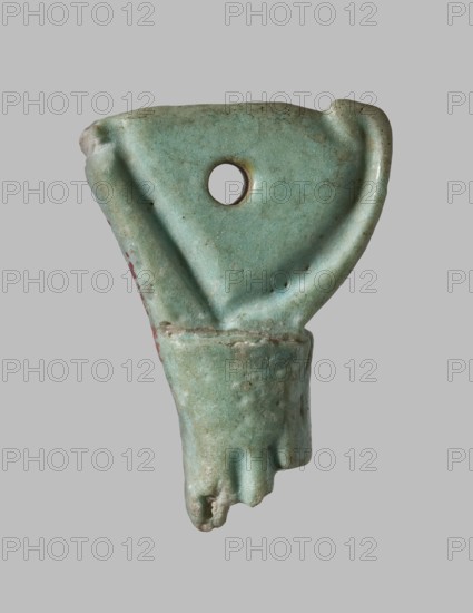 Amulet in the shape of a crown of Lower Egypt. Between the back of the crown and the rod, a plane pierced with a hole., Late Period, 26th Dynasty, Egypt, 664–525 BC. Amulet; height 2.7 cm, width 1.3 cm., An irregularly shaped turquoise-green ceramic fragment with a rounded top edge and a hole near the upper center; the surface shows subtle darker speckles and worn areas, with a curved ridge along one side and a rounded protrusion at the lower end that appears broken; there are a few small spots of reddish discoloration on one side and the background is a uniform light gray.