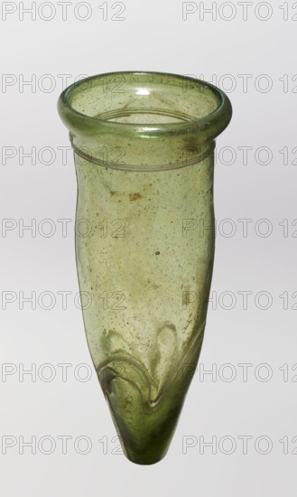 Lamp oil container, glass with cream enamel thread, 12th–15th century, possibly Syria or Egypt Middle East, Islamic/Arabic, oil lamp, height 12.0 cm, diameter 5.2 cm., A translucent green glass vessel with a rounded flared rim and a long tapering body, showing a bubbly texture and some cloudy inclusions throughout; the rim is a darker green band while the body is a lighter yellow-green with subtle brownish spots and streaks, and near the pointed end there are raised swirl-like ridges in the glass; the background is plain and pale.